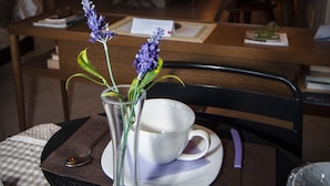 A dining table with a checkered tablecloth, a white cup and saucer, a clear vase with lavender flowers, and a black chair. - Passeggiate Romane B&B (Rome)