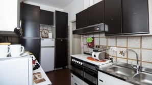 A compact kitchen with a refrigerator, stove, sink, and cabinets. - Passeggiate Romane B&B (Rome)
