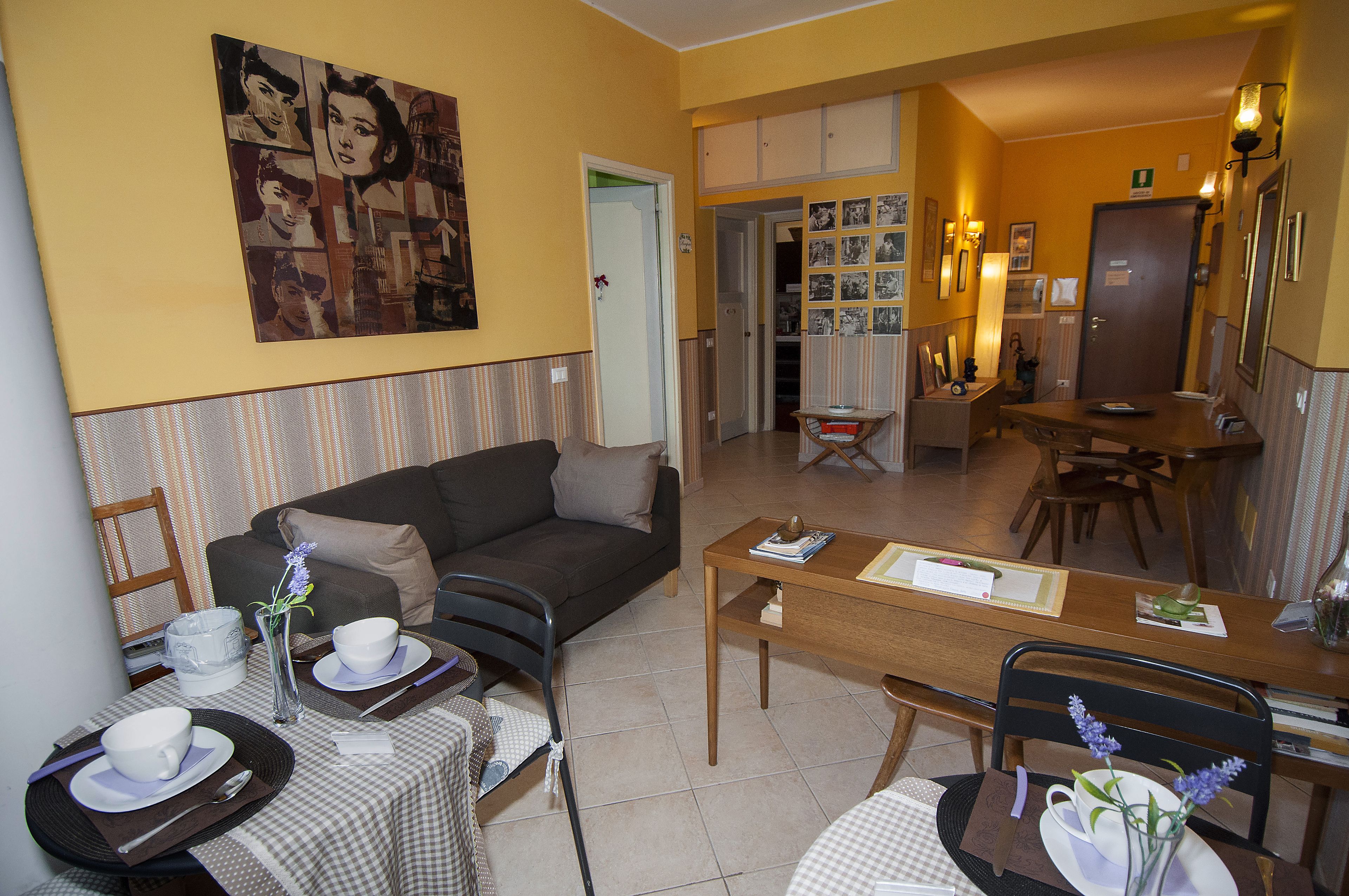 A living room with a sofa, dining table, and chairs. There is a painting on the wall and a door leading to another room.