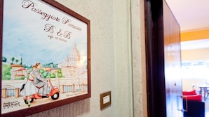 A framed artwork on a wall depicting a couple on a scooter, with a cityscape background. - Passeggiate Romane B&B (Rome)
