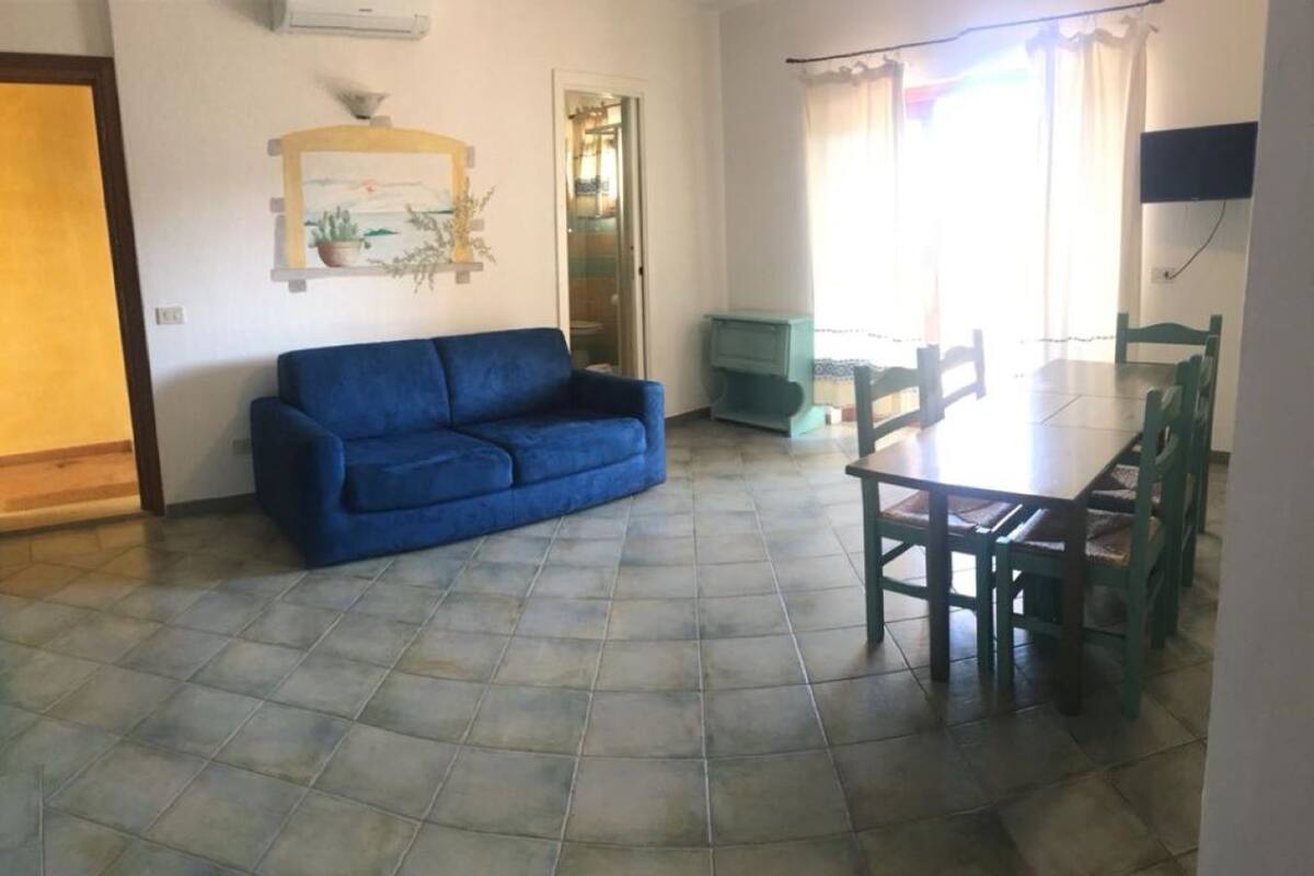 Un salon avec un canapé bleu, une table à manger avec des chaises et un sol carrelé.