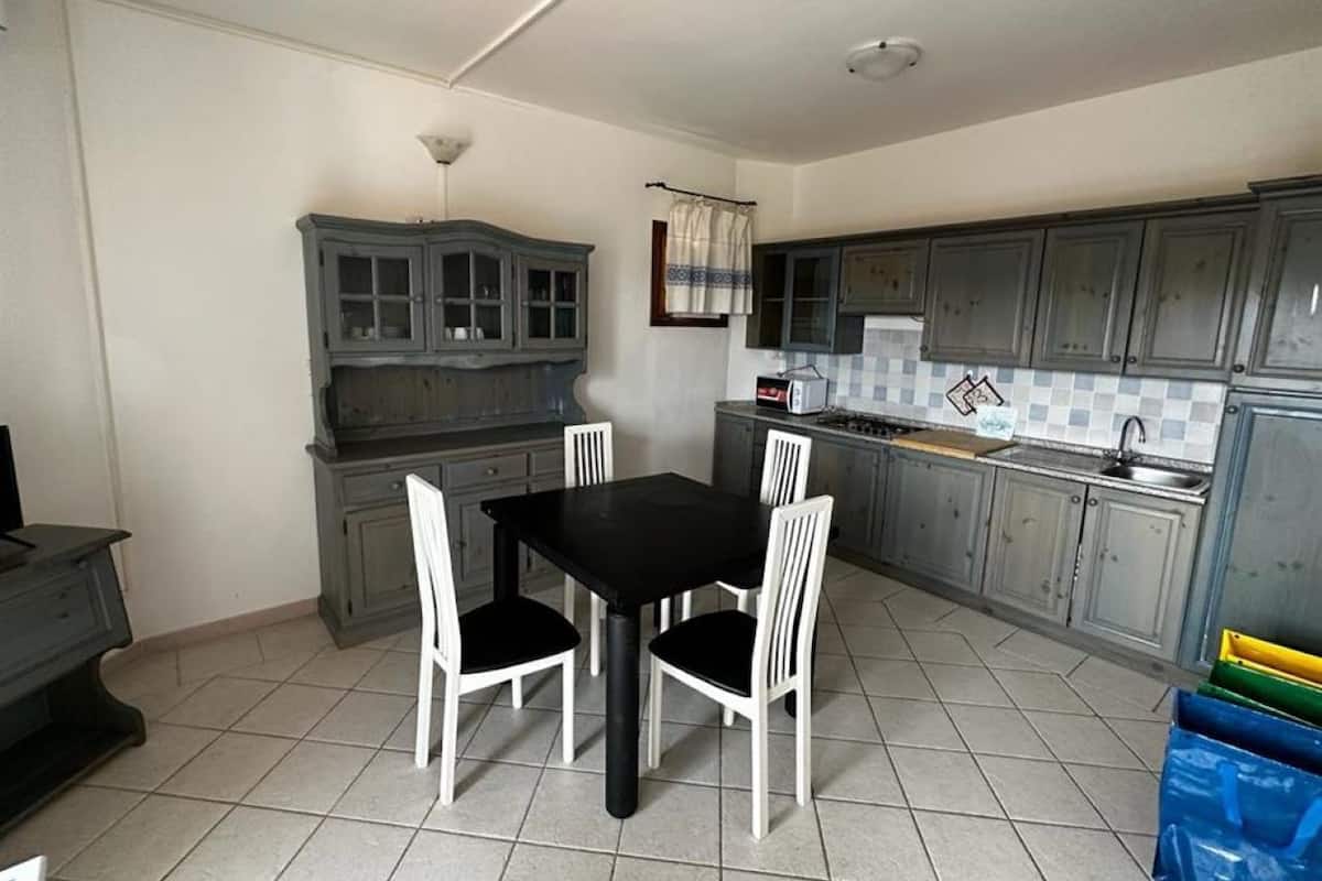 Une cuisine compacte avec une table et des chaises, des meubles de couleur grise et un sol carrelé.