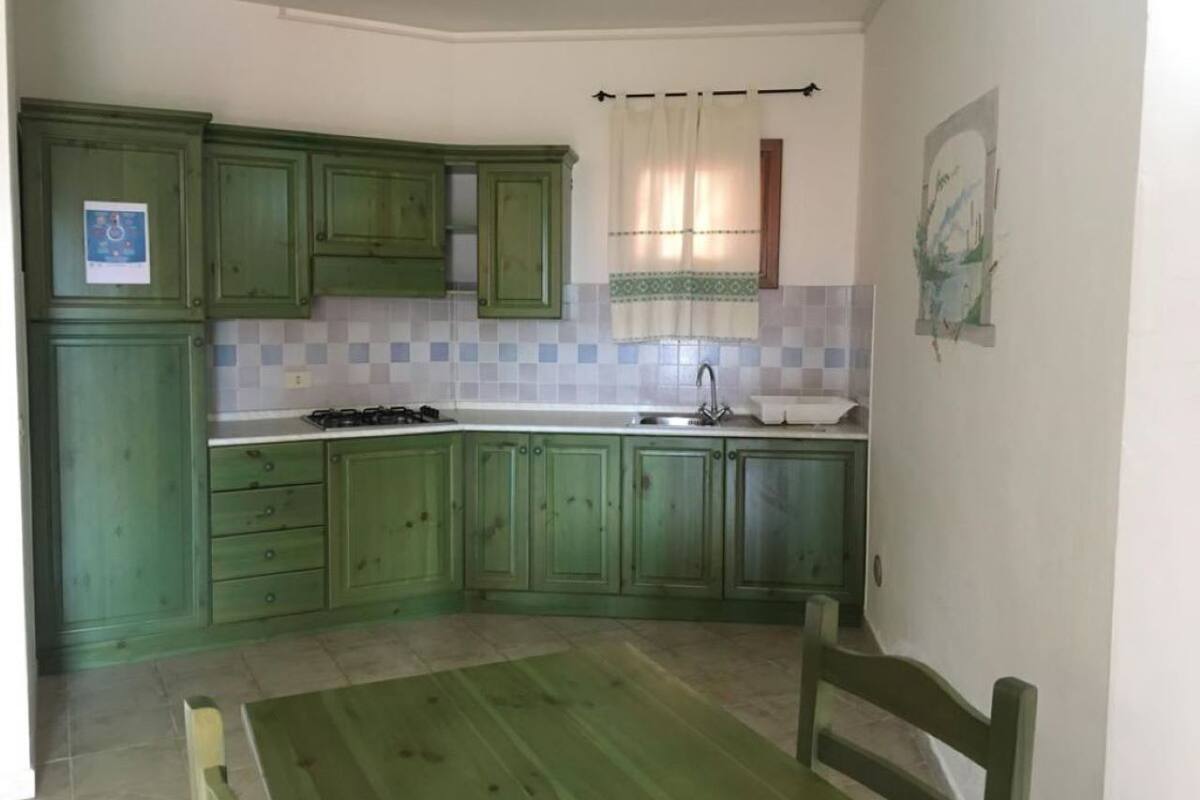 Une cuisine avec des meubles de couleur verte, un évier et une fenêtre avec un rideau.