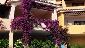 Un edificio con un balcone fiorito di fiori viola, un tetto in tegole e un cielo azzurro.