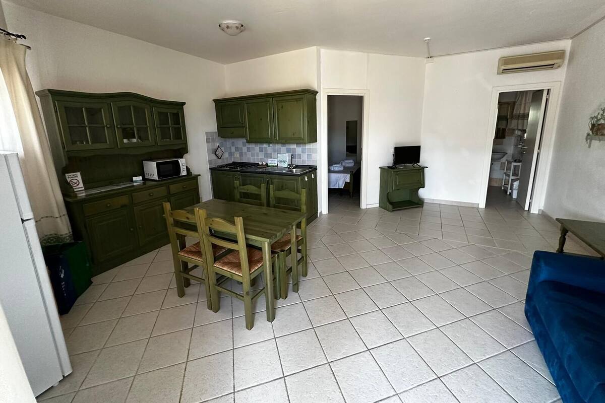 Une cuisine de taille réduite avec des meubles de couleur verte, une table à manger avec des chaises et un canapé bleu.