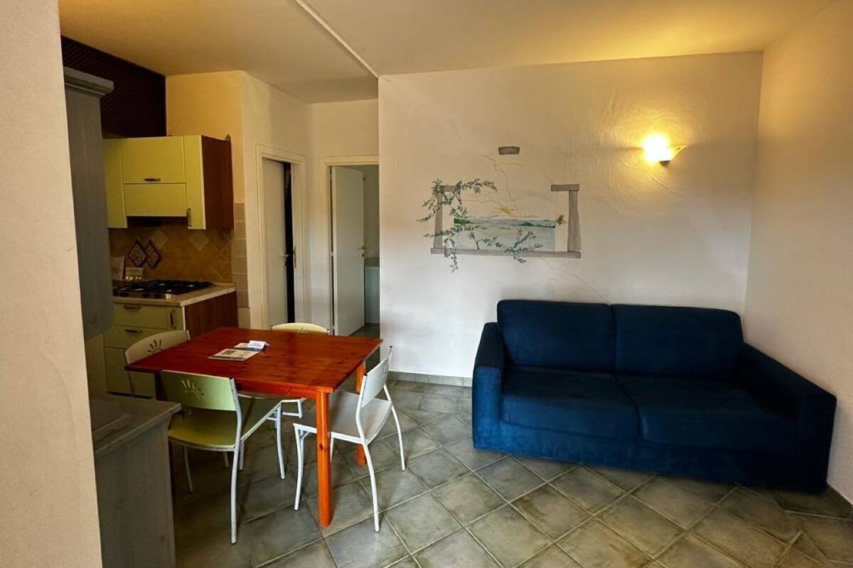 Un espace de vie compact comprenant une table et des chaises, un canapé bleu et un coin cuisine avec des placards et une cuisinière.