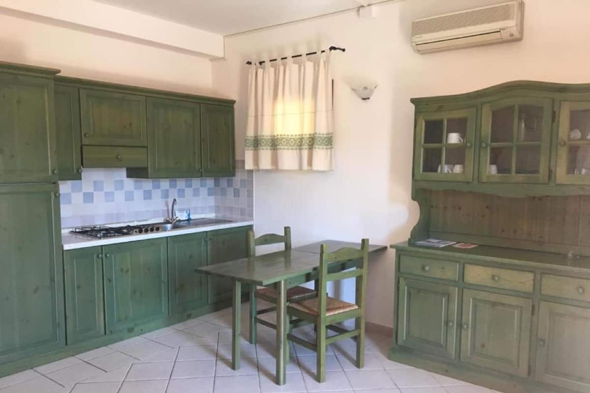Une cuisine avec des meubles de rangement verts, une table à manger et des chaises.