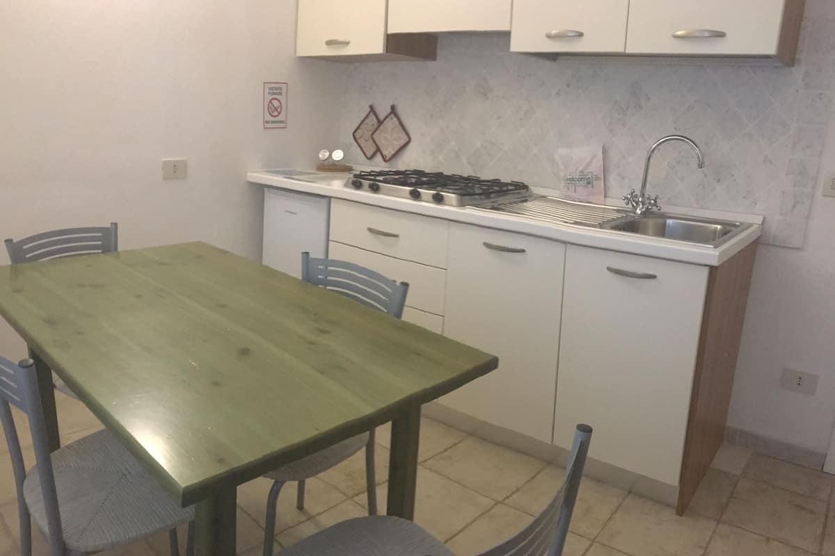 Une cuisine de taille réduite avec des meubles blancs, une cuisinière à gaz, un évier et une table à manger avec des chaises.