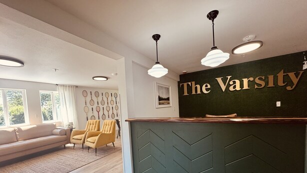 A reception area with a green wall, a reception desk, and a seating area with a sofa and chairs. - Varsity North (Centralia)