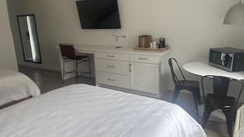 A hotel room with a bed, a desk with a chair, a TV, a microwave, and a small table.