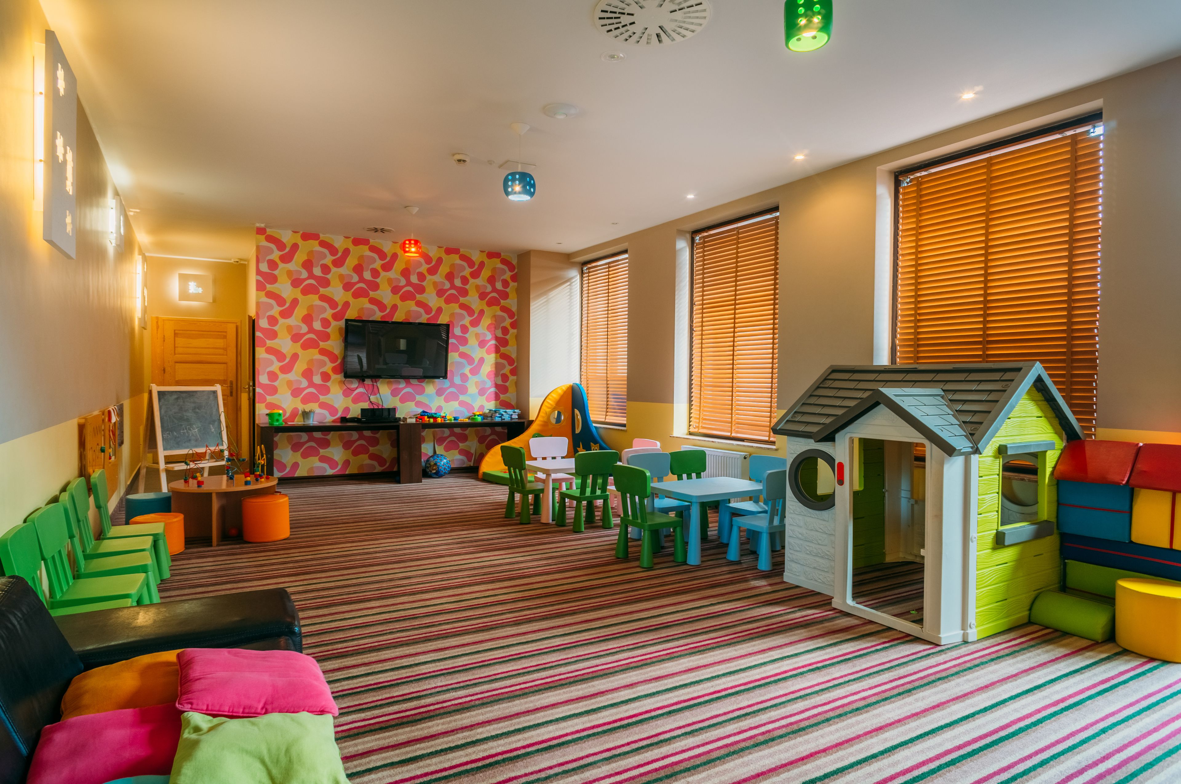 A children's playroom with colorful furniture, a playhouse, and a television on the wall.