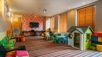 A children's playroom with colorful furniture, a playhouse, and a television on the wall.