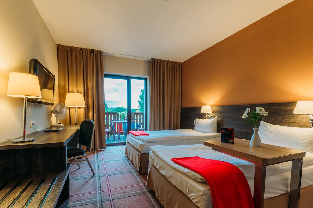 Quarto de hotel com duas camas, uma escrivaninha, uma cadeira, uma mesa e vista para o exterior.