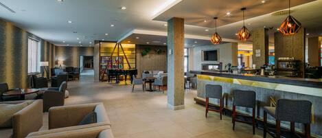 A spacious lobby with a bar area, seating arrangements, and a piano.