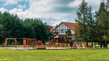 A playground with various play structures, a building with a red roof, and a grassy field.