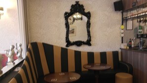 Un coin bar agrémenté d’un miroir à cadre noir, d’un canapé à rayures et de deux petites tables rondes.