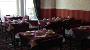 Un espace repas avec des tables dressées pour le service, où les nappes et les chaises sont disposées de manière uniforme.