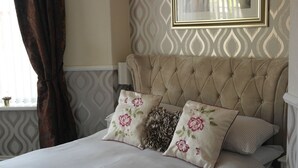 Une chambre à coucher avec une tête de lit capitonnée, des coussins à motifs floraux et un papier peint à motifs.