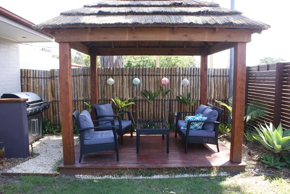 A covered patio with two wicker chairs and a table, surrounded by bamboo fencing and decorative lanterns. - Karuah Riverside Motel (Karuah)