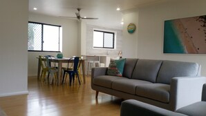 A modern living room with a grey sofa, a dining table with colorful chairs, and a kitchen area in the background. - Karuah Riverside Motel (Karuah)