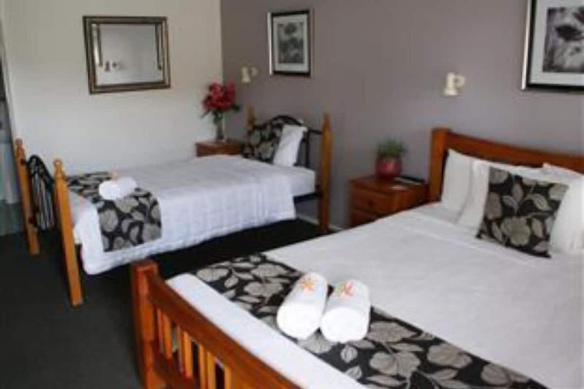 Una habitación de hotel con dos camas individuales, un cabecero de madera, una mesita de noche con lámpara y cuadros enmarcados en la pared.