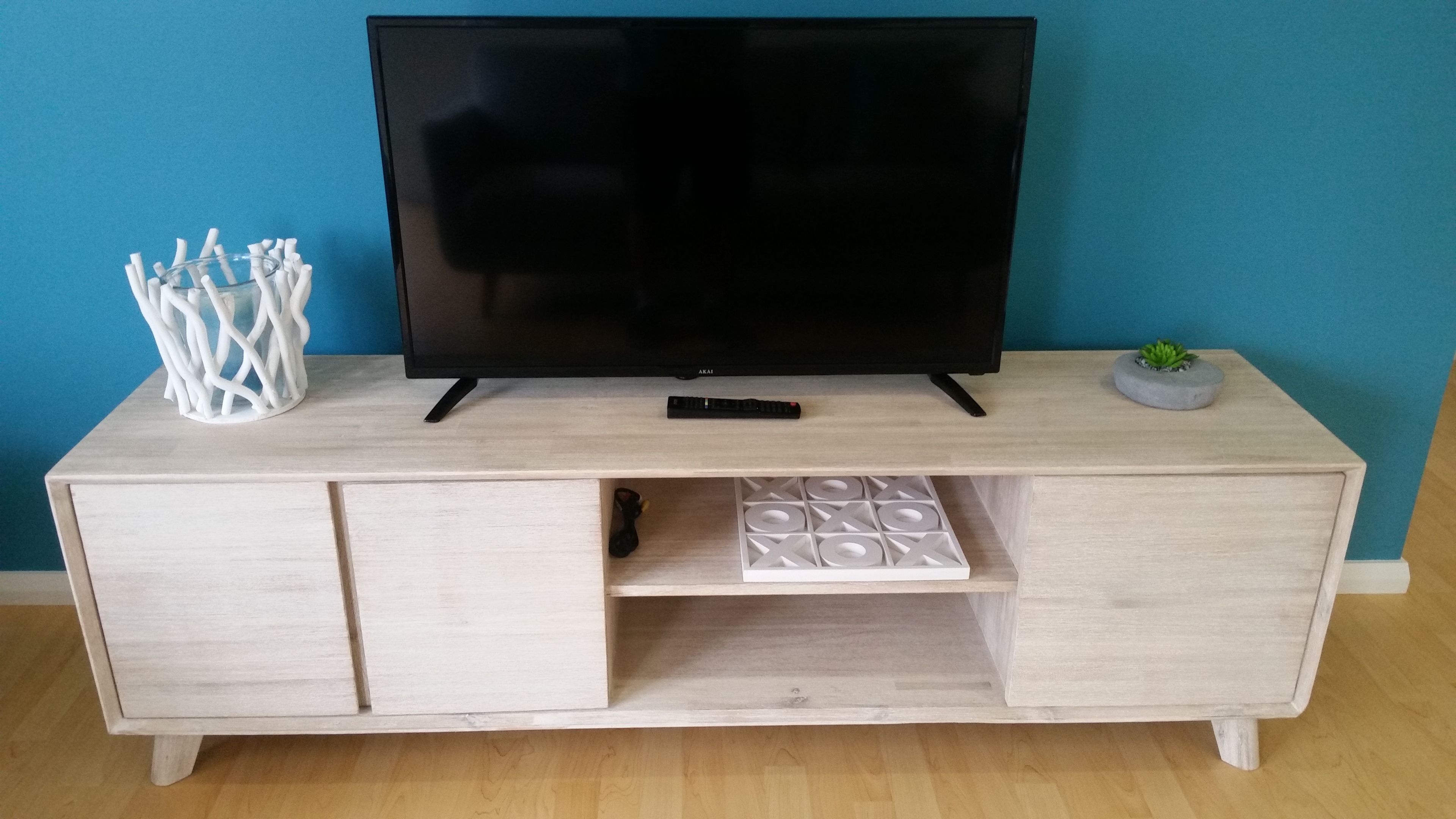 A wooden TV stand with a flat-screen TV, a remote control, and a small plant.