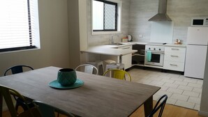 A modern kitchen with white appliances, a window with a decorative screen, and a dining area with a table and chairs. - Karuah Riverside Motel (Karuah)