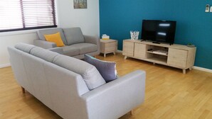 A living room with a grey sofa, a small side table, a TV stand, and a blue accent wall. - Karuah Riverside Motel (Karuah)