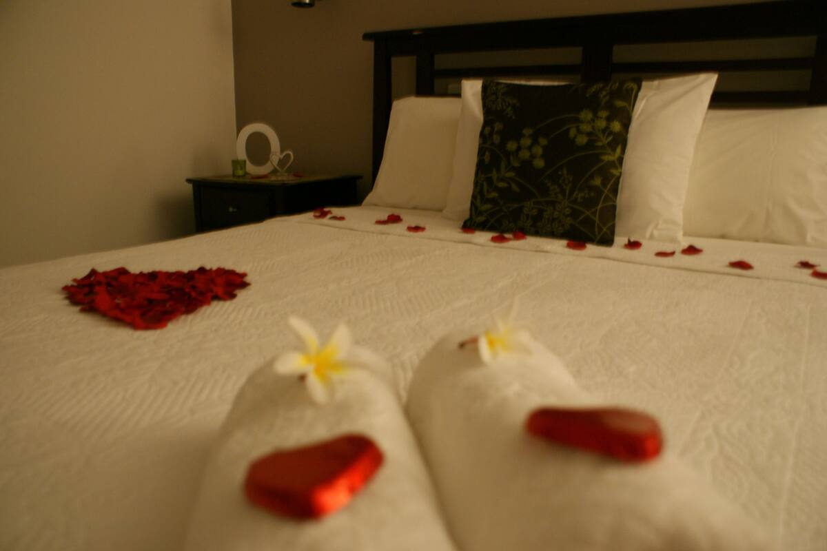 A bed with rose petals and heart-shaped pillows.