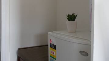 A compact room with a small bench, a potted plant, and a white refrigerator.