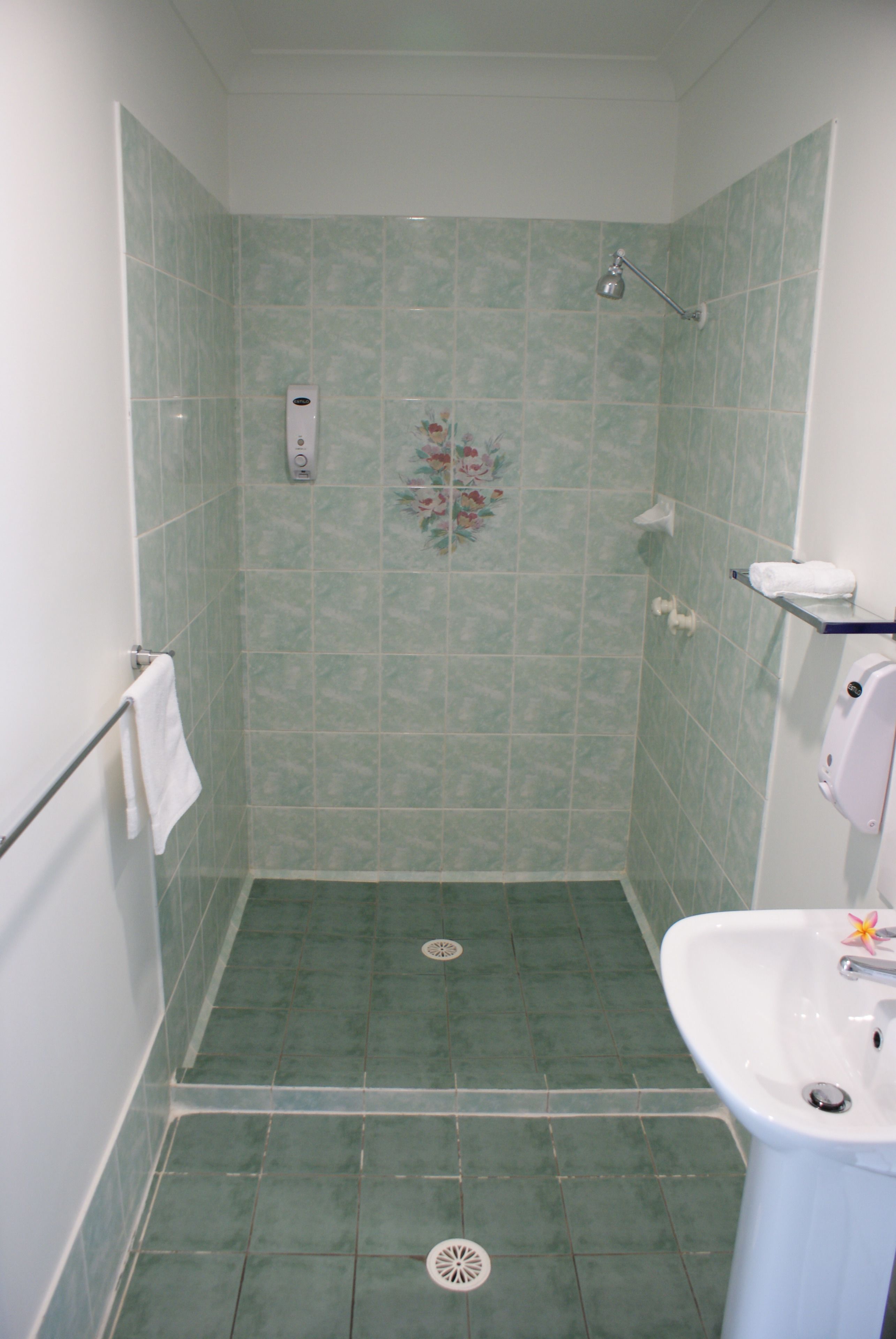 A bathroom with green tiles, a shower, a sink, and a towel rack.