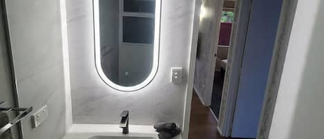 A modern bathroom with a white sink, a round mirror with integrated lighting, and a wooden floor.