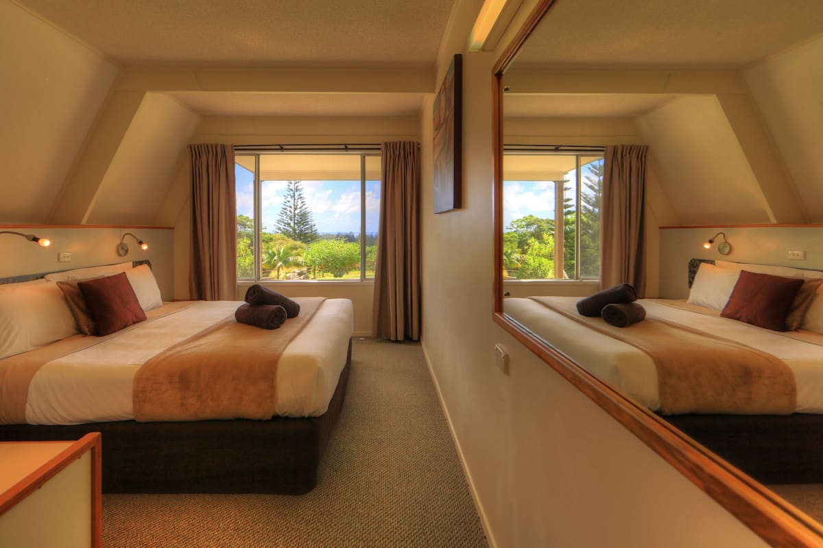 A hotel room with two beds, a large mirror, and a view of greenery outside.