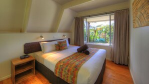 Ein Schlafzimmer mit Bett, Nachttisch, einem Fenster mit Vorhängen und Blick ins Grüne.
