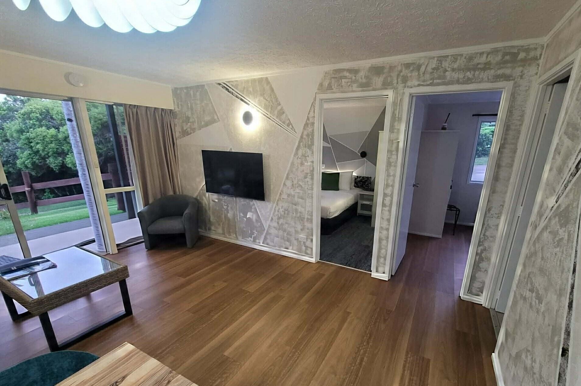 A spacious living room with a large TV, a comfortable chair, and a glass table.