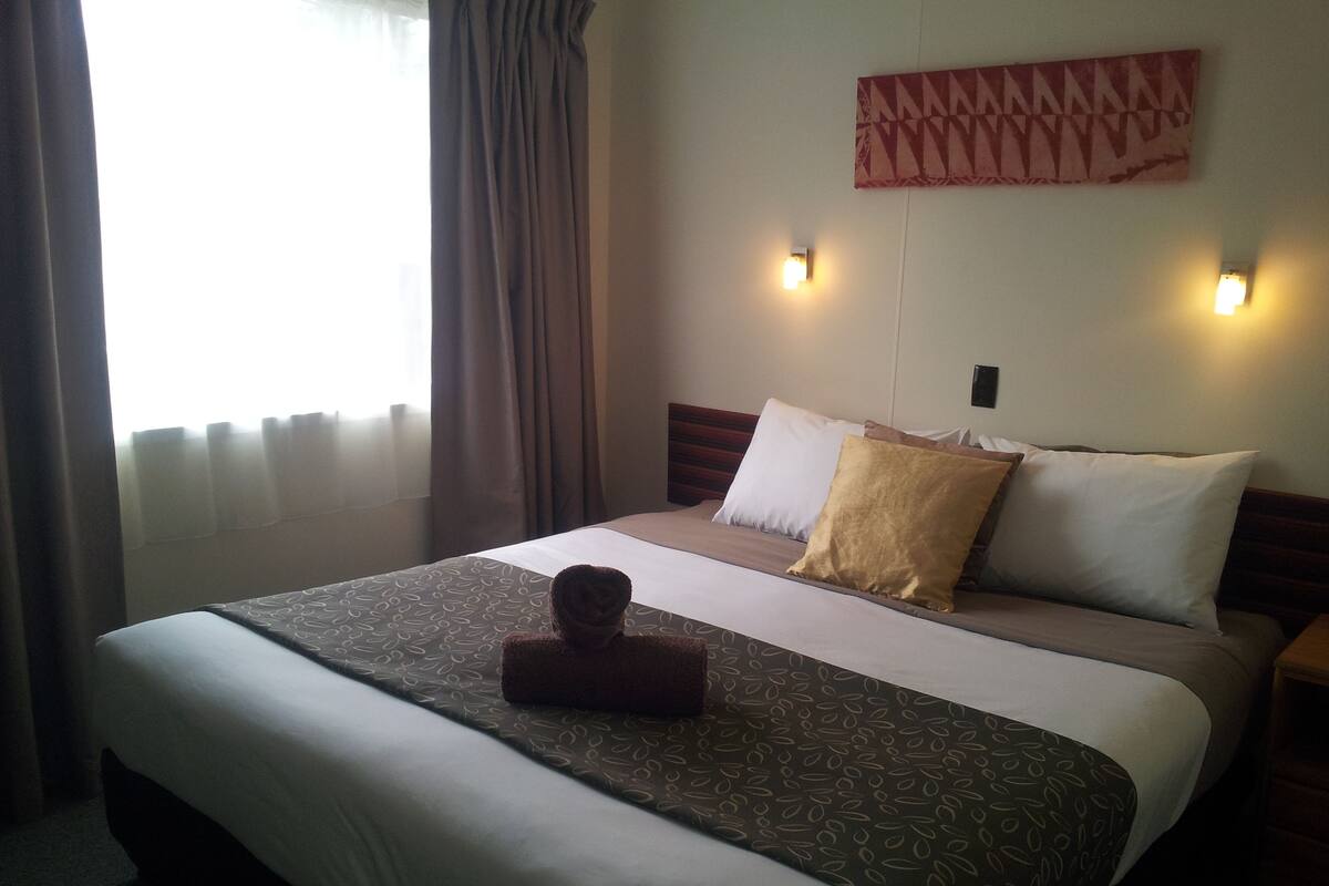 A hotel room with a neatly made bed, a headboard with a geometric pattern, and two wall-mounted lights.