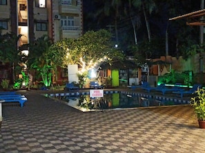 A pool area with a closed sign, lounge chairs, and a tiled walkway.