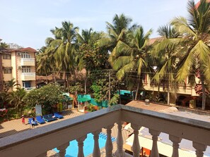 A pool area with blue lounge chairs, surrounded by palm trees and buildings. - Resort Park Avenue (Calangute)