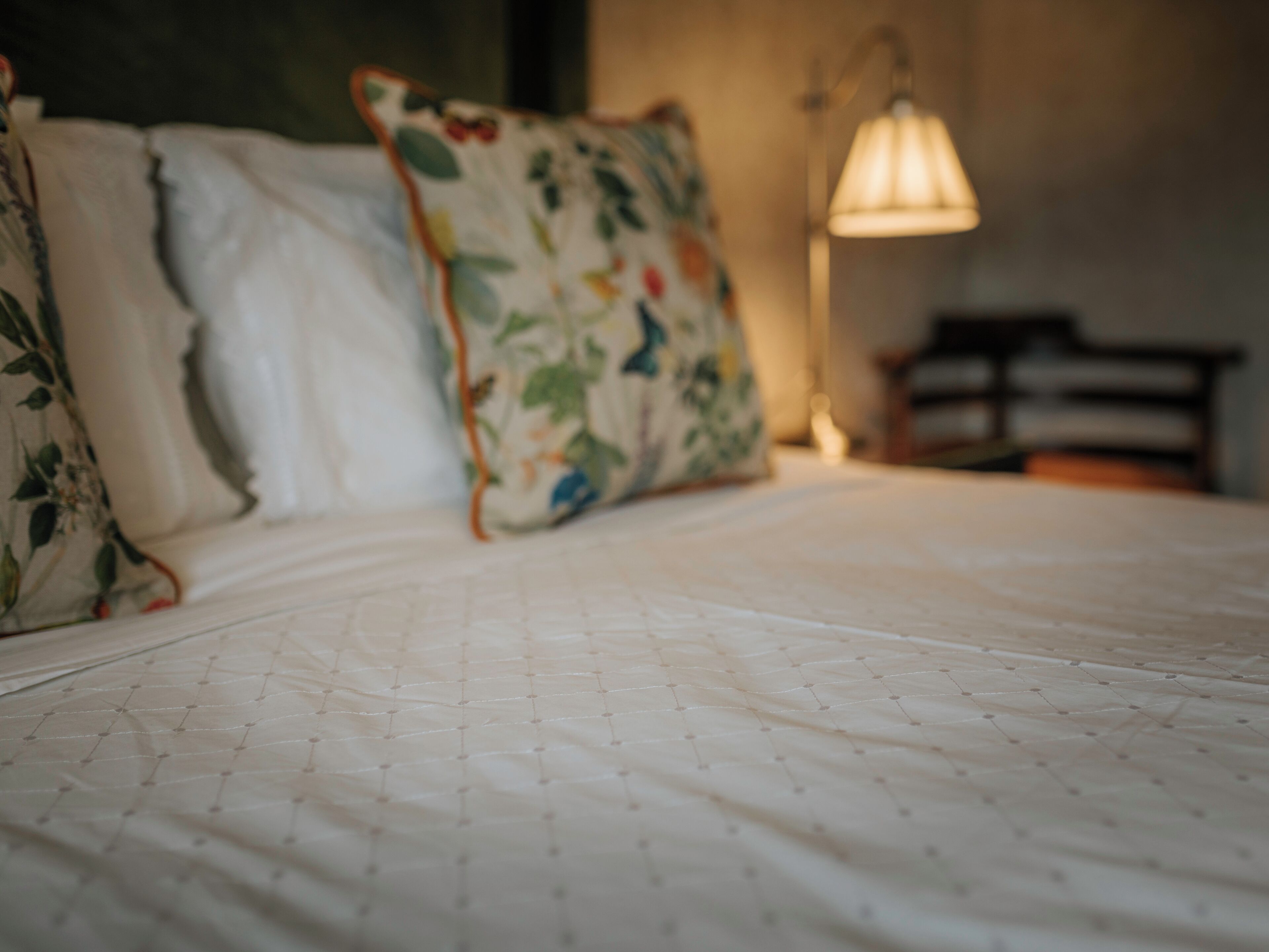 A bed with a quilted pattern and floral pillows.