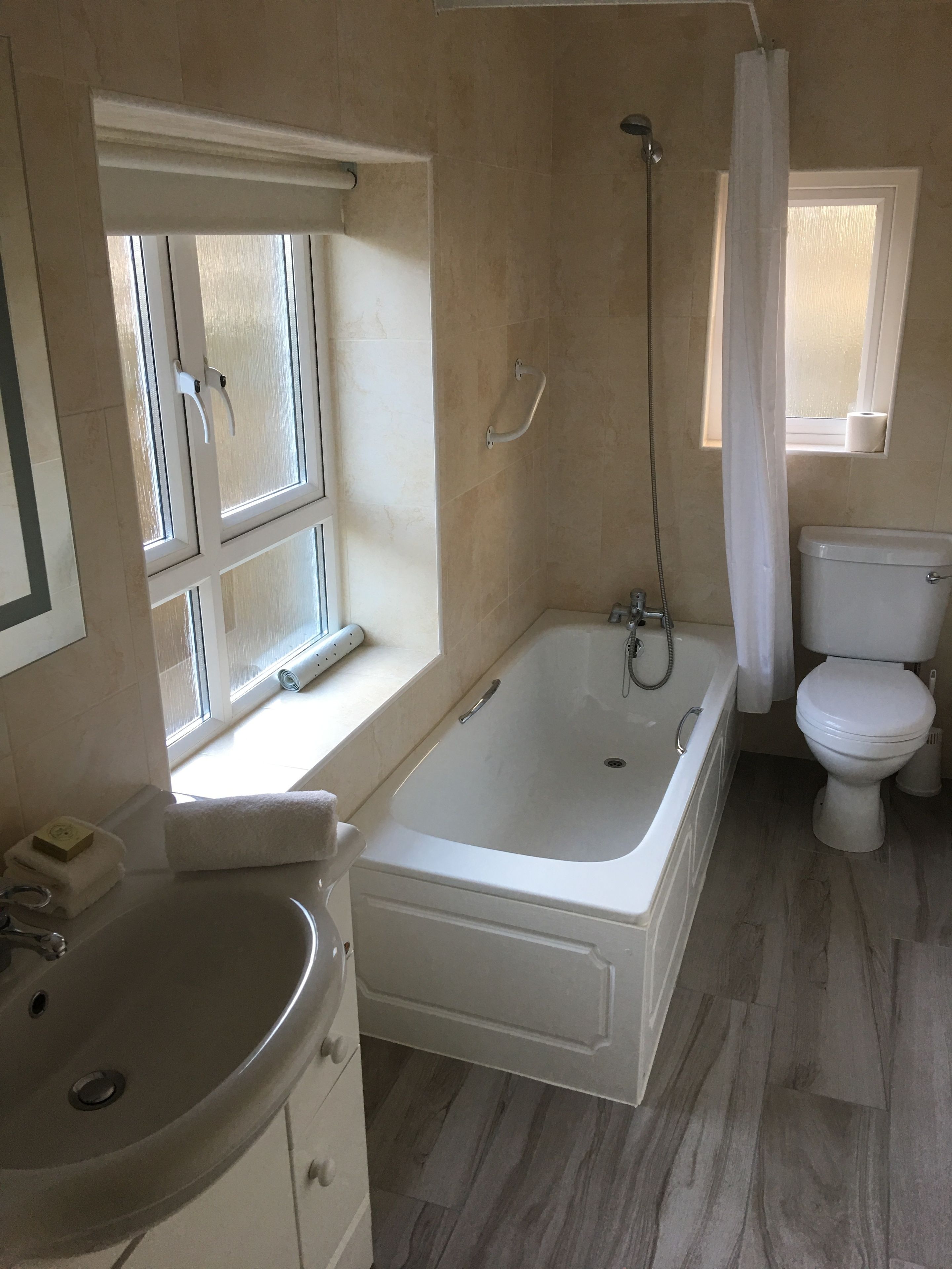 Un baño con bañera, inodoro, lavabo y ventana con cortina.