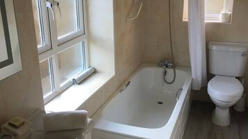 Un baño con bañera, inodoro, lavabo y ventana con cortina.