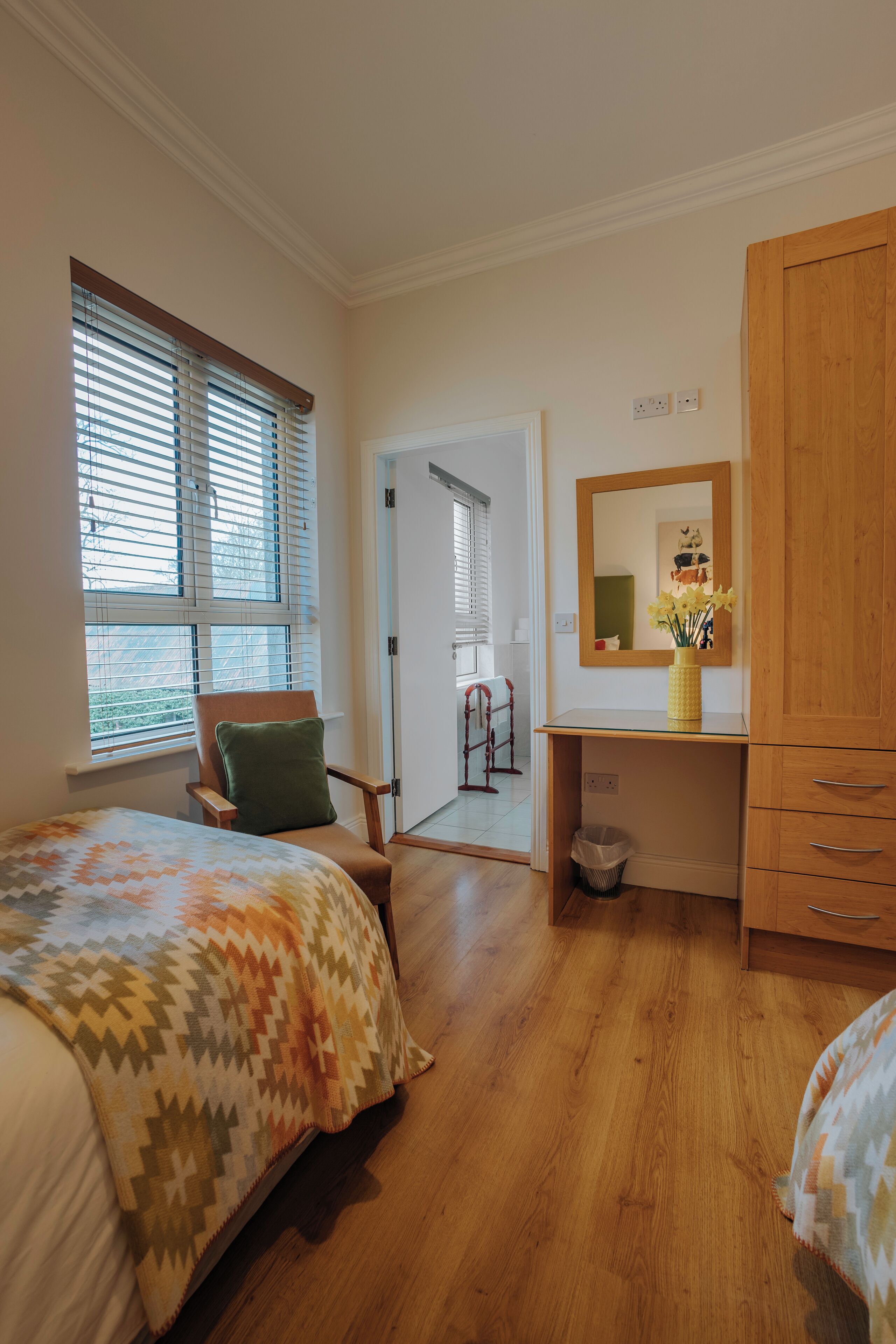Une chambre à coucher comprenant un lit, une chaise, un bureau avec un miroir et un vase, ainsi qu’une armoire.