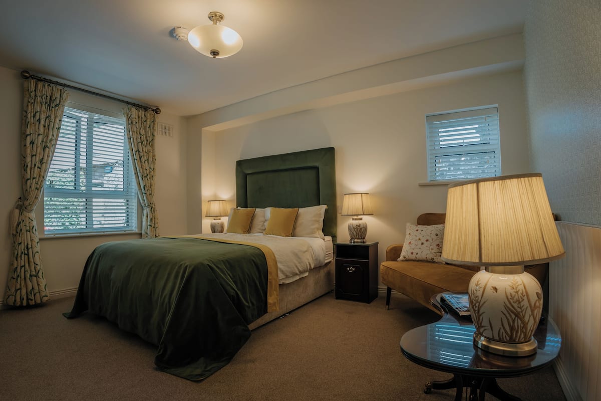 A hotel room with a bed, bedside lamps, a nightstand, a chair, and a table with a lamp.