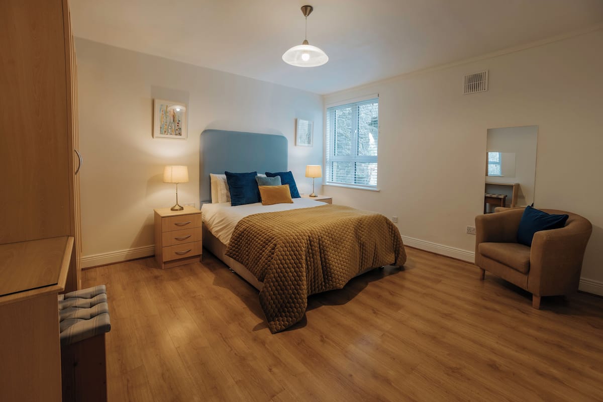 A bedroom with a bed, bedside tables, a chair, a window, and a ceiling light.