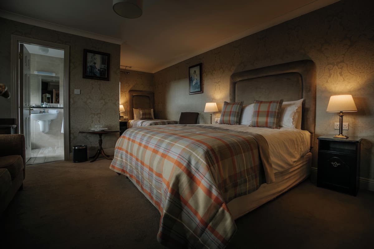 A bedroom with a large bed, two bedside tables with lamps, a small table with a lamp, a chair, and a door leading to a bathroom.