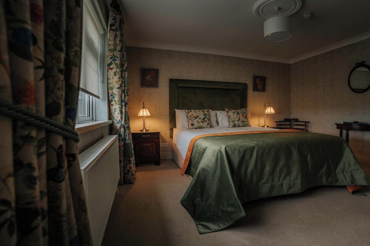 A bedroom with a bed, two bedside tables, a nightstand, a dresser, and a window with curtains.