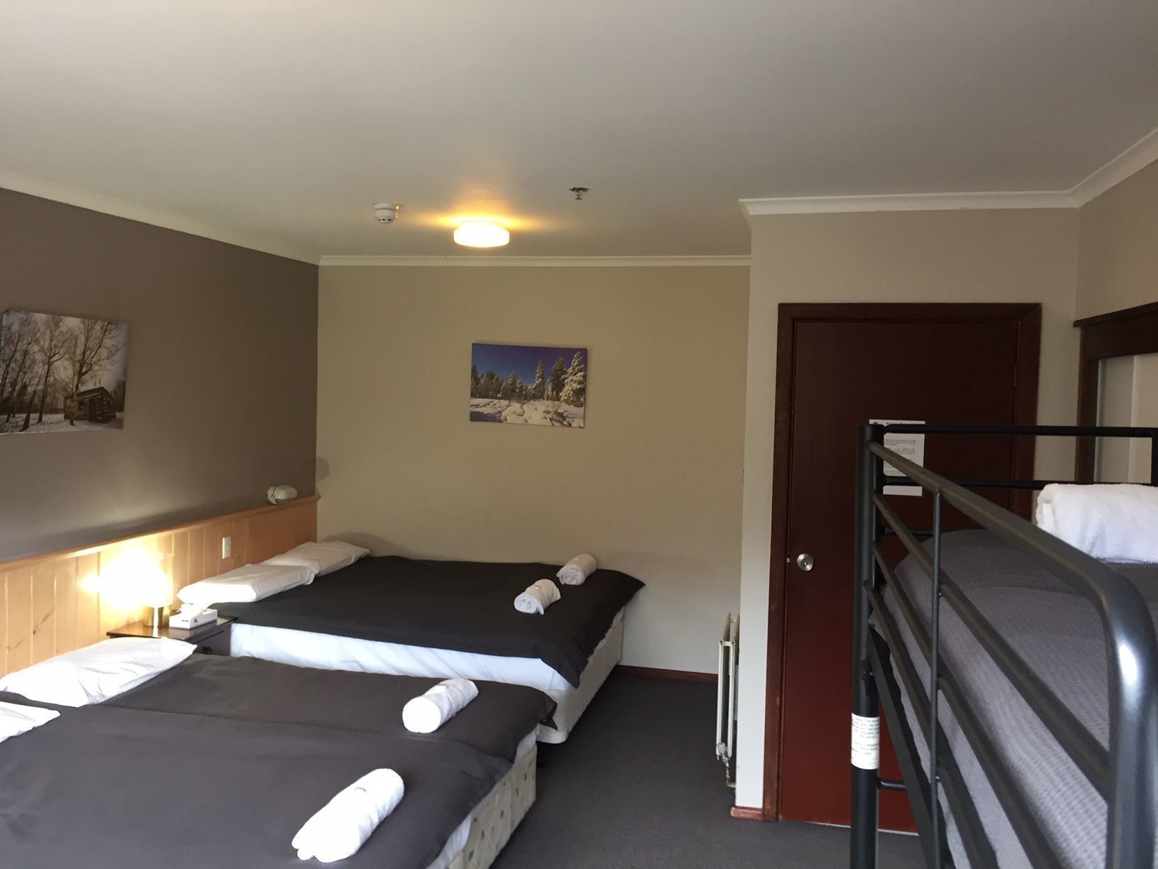 Quarto de hotel com duas camas, cabeceira de madeira, um quadro na parede e uma porta.