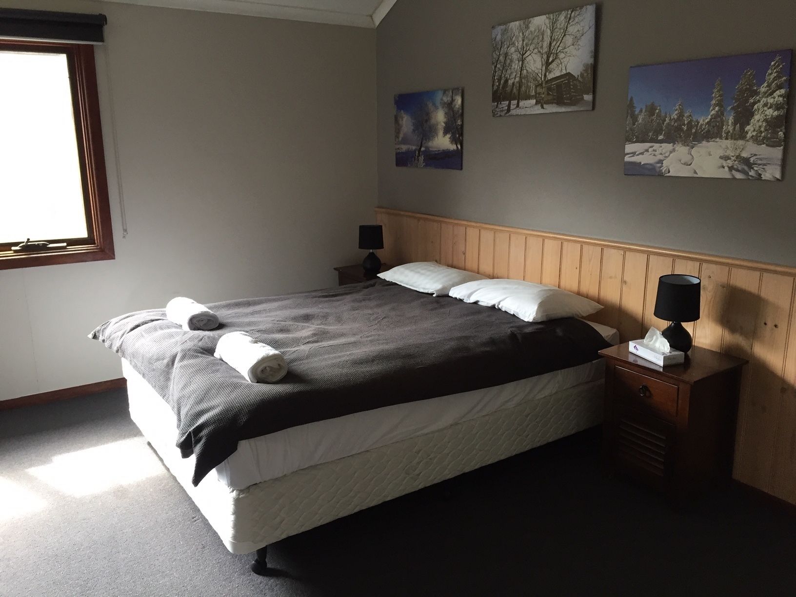 A neatly made bed with rolled towels, a bedside lamp, and a nightstand with a tissue box.