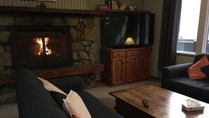 Una sala de estar con chimenea de piedra, televisor de pantalla plana, sofás oscuros y una mesa de centro de madera.