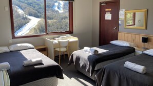 Habitación de hotel con dos camas, un escritorio y un ventanal con vistas a un río y un bosque.